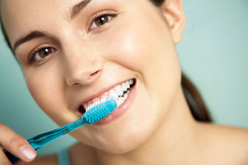 Woman smiling with all on 4 dental implants and brushing her teeth at Surf City Oral and Maxillofacial Surgery in Huntington Beach, CA