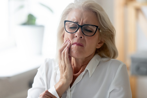 Woman wincing with pain in jaw due to TMD diagnosed by Surf City Oral and Maxillofacial Surgery in Huntington Beach, CA